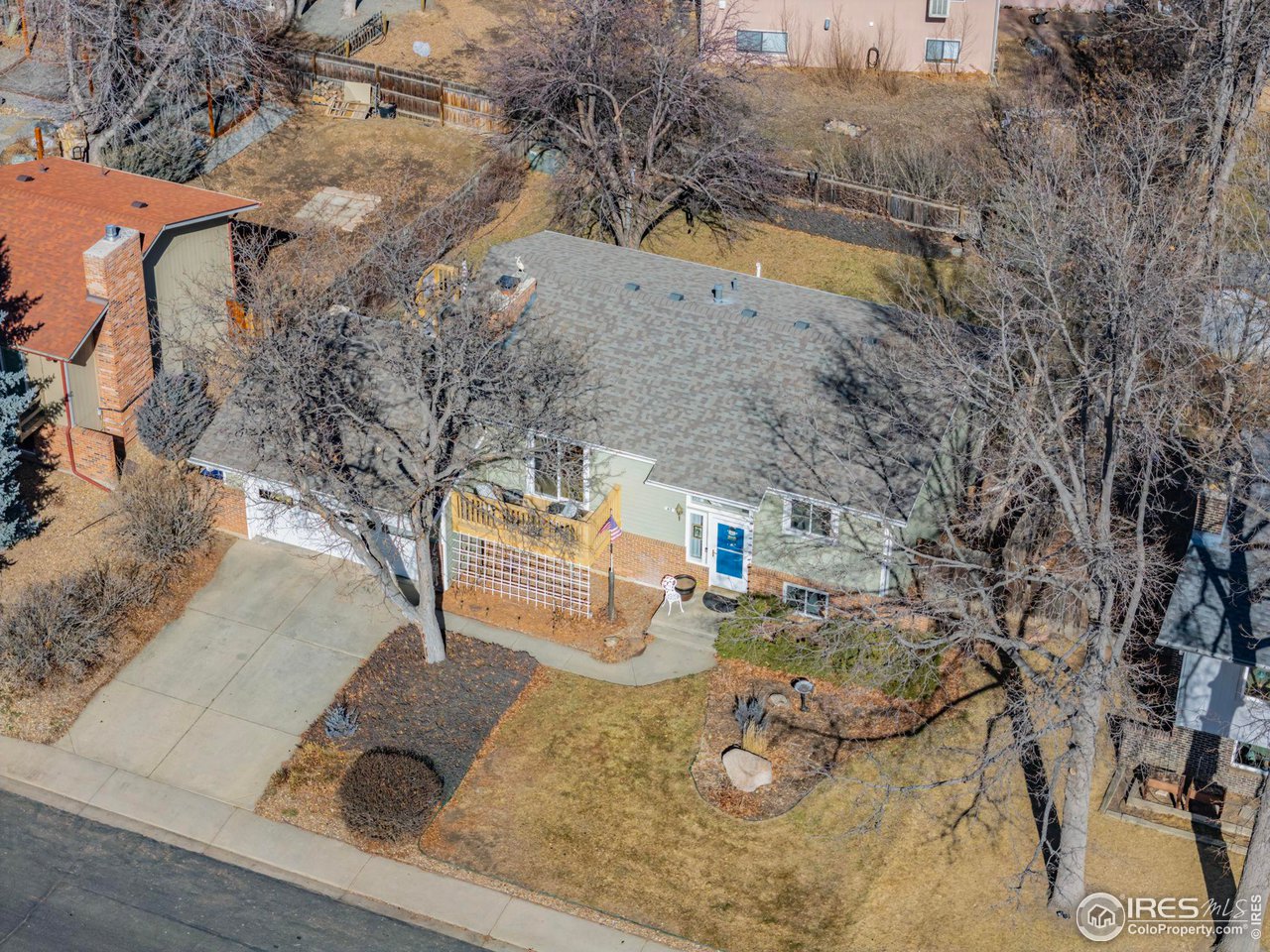 Aerial view of a single-story home with a broad gray roof, driveway, and leafless front yard.