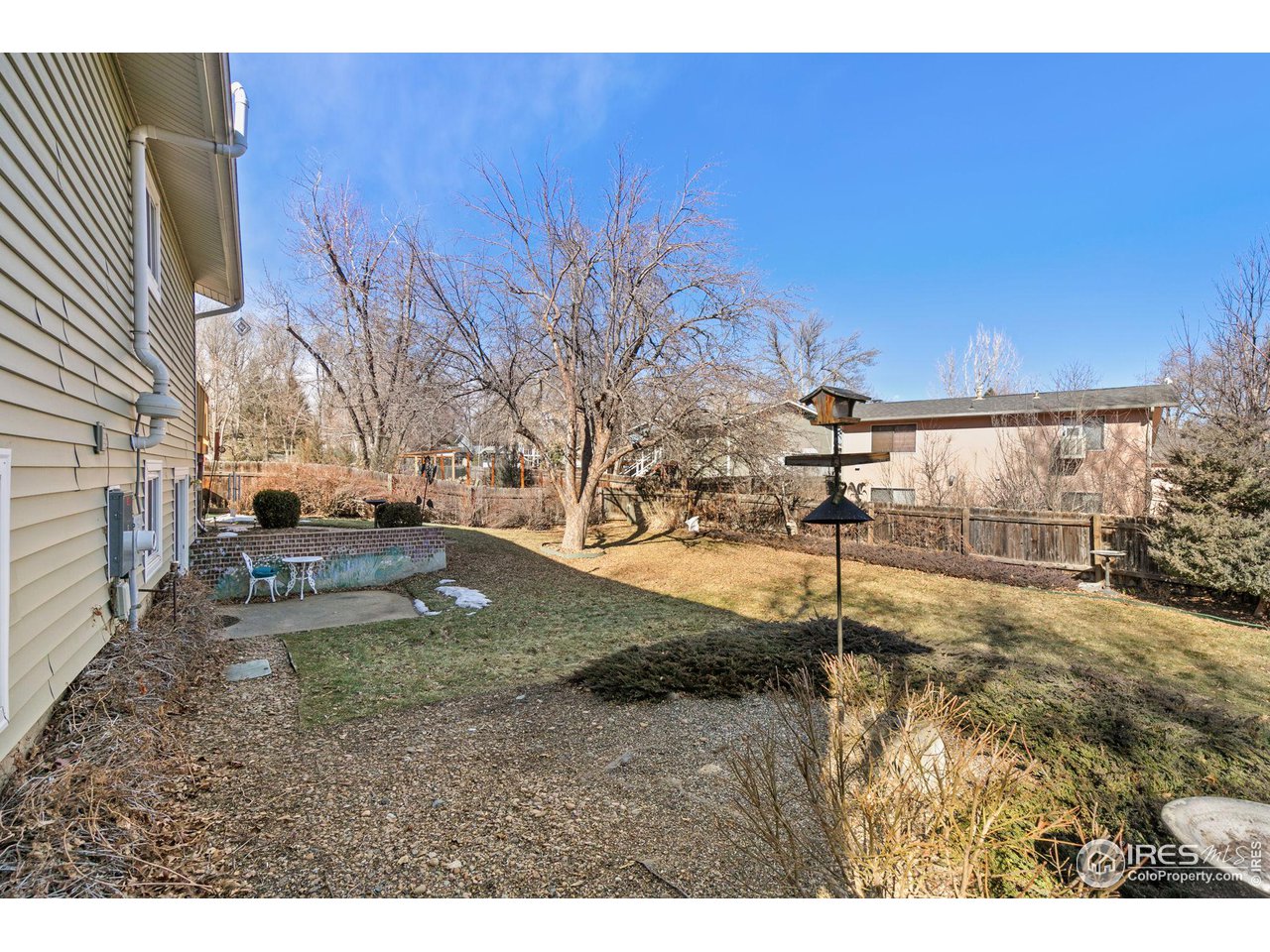 Backyard with leafless trees, a small patio, bird feeder, and patches of snow.