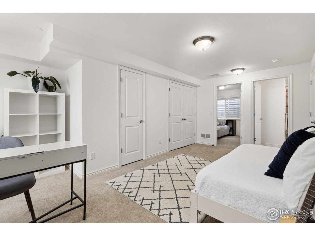 Bedroom with a white bed, geometric rug, and desk beside built-in shelving.