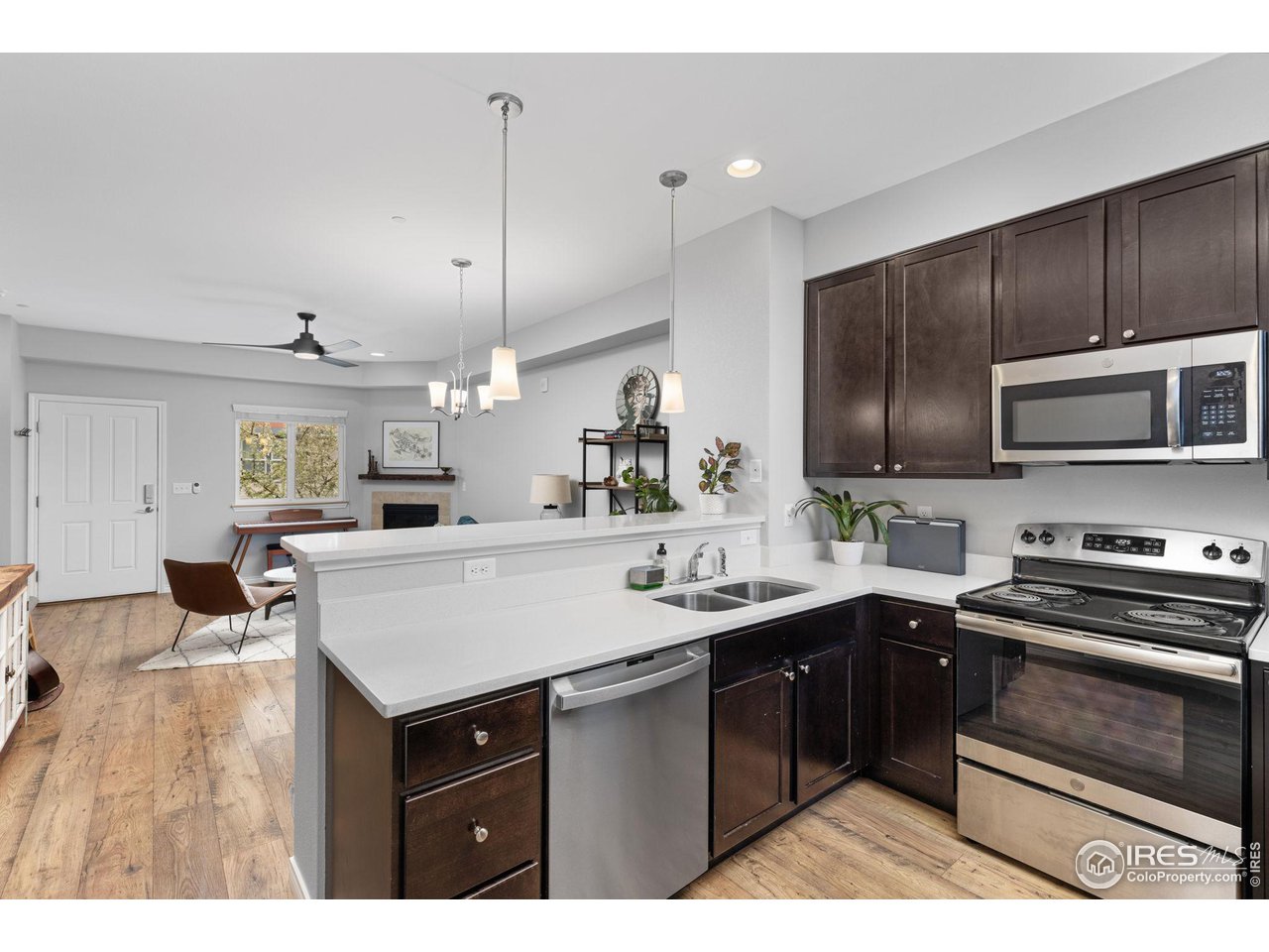 Open-plan kitchen with dark cabinets, white counters, and stainless steel appliances beside a furnished living area.