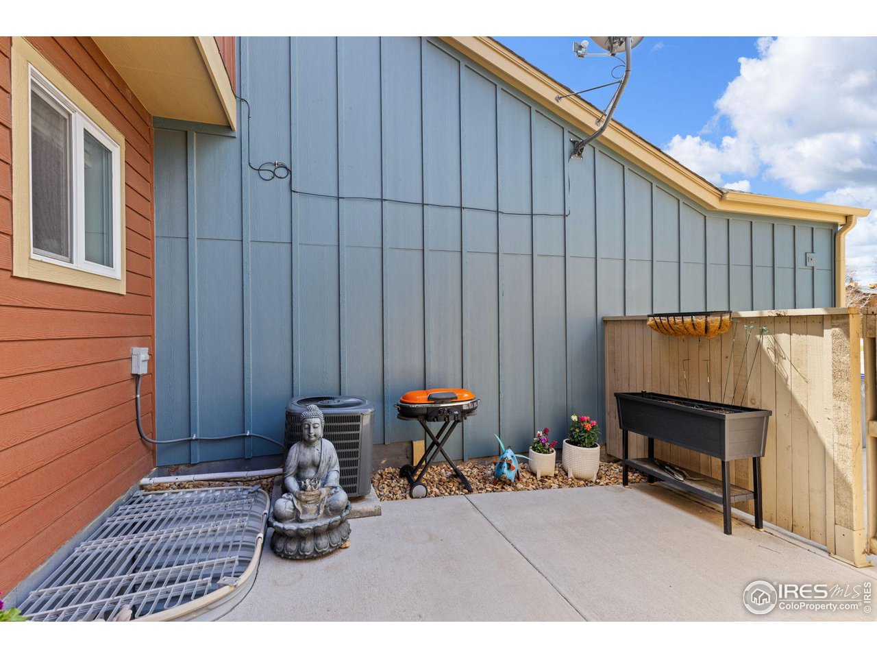 Concrete patio beside blue siding, with raised planters and a Buddha statue.