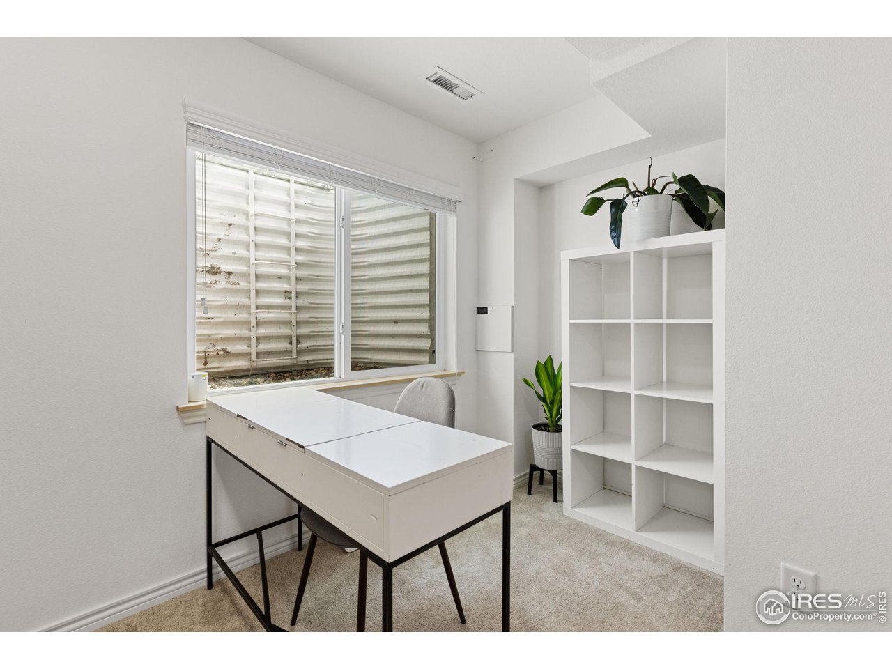 Home office with a white desk, cube shelving, and a large window with blinds.