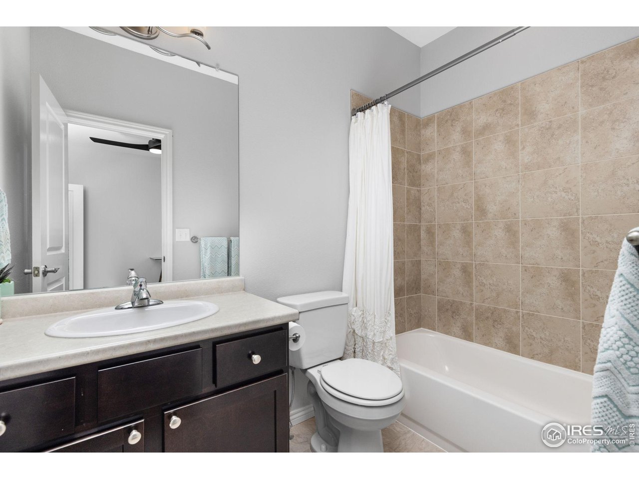 Bathroom with a dark wood vanity, white fixtures, and beige tile around the bathtub.