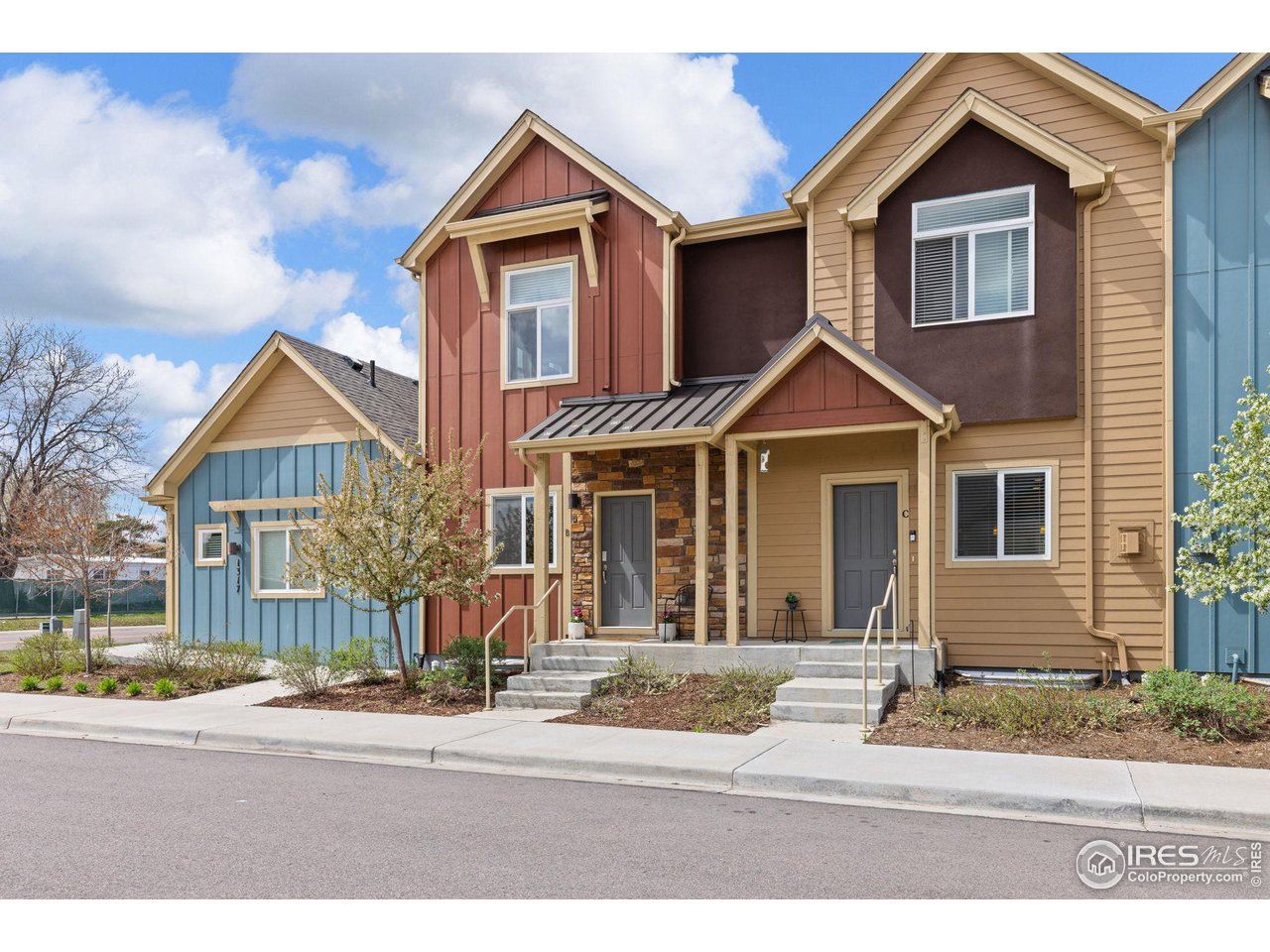 Townhouse exterior with tan and reddish-brown siding, stone entry accent, and front steps.