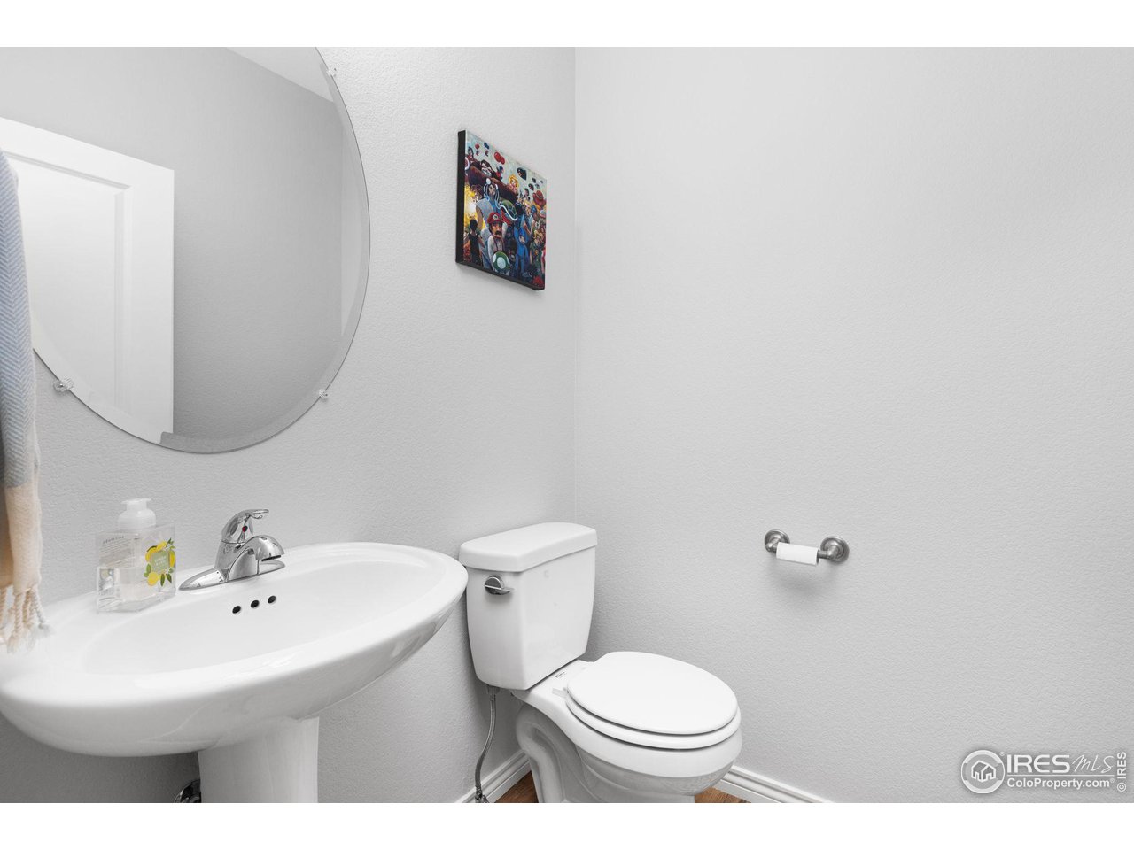 Bathroom with a pedestal sink, large round mirror, and toilet.