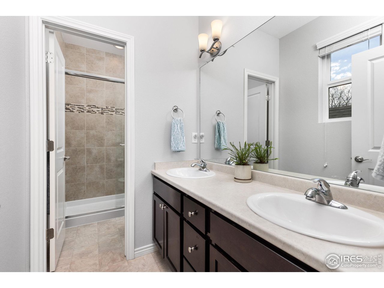 Bathroom with a double-sink vanity and a tiled shower behind a glass door.