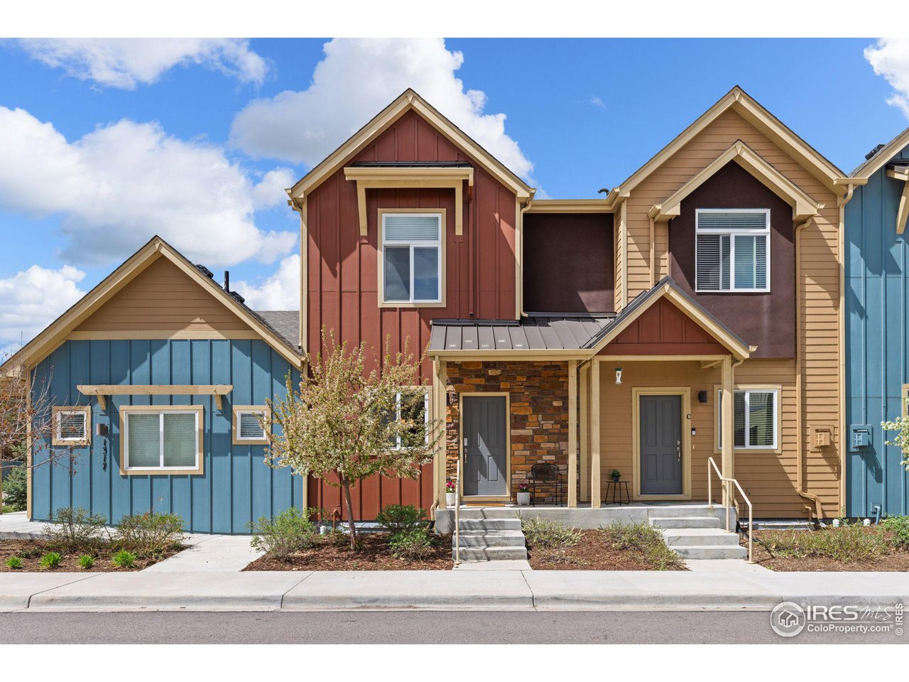 Attached townhome with red and tan siding, a stone entry, and a small landscaped front yard.