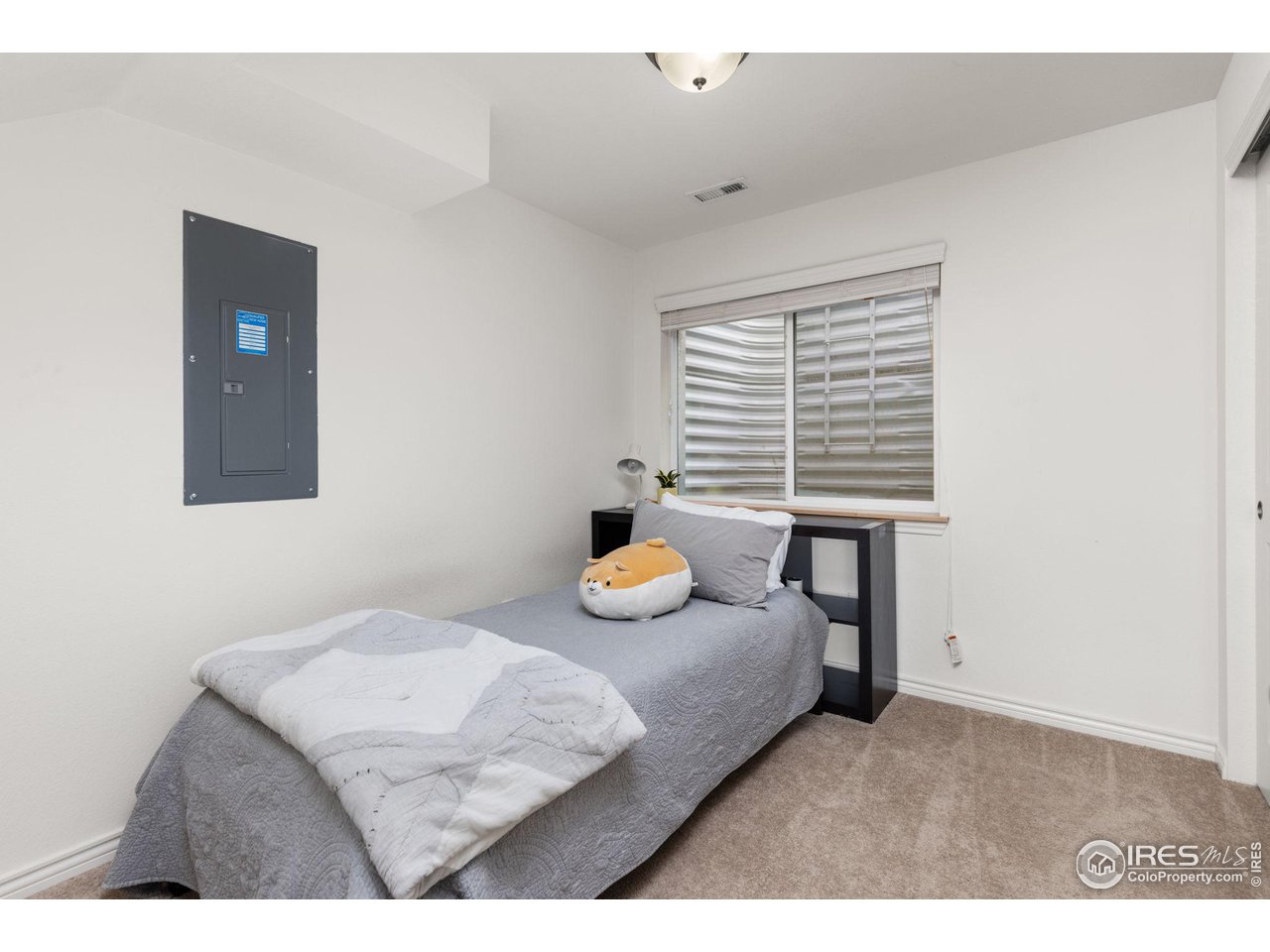 Furnished bedroom with a single bed, gray bedding, and a window with blinds.