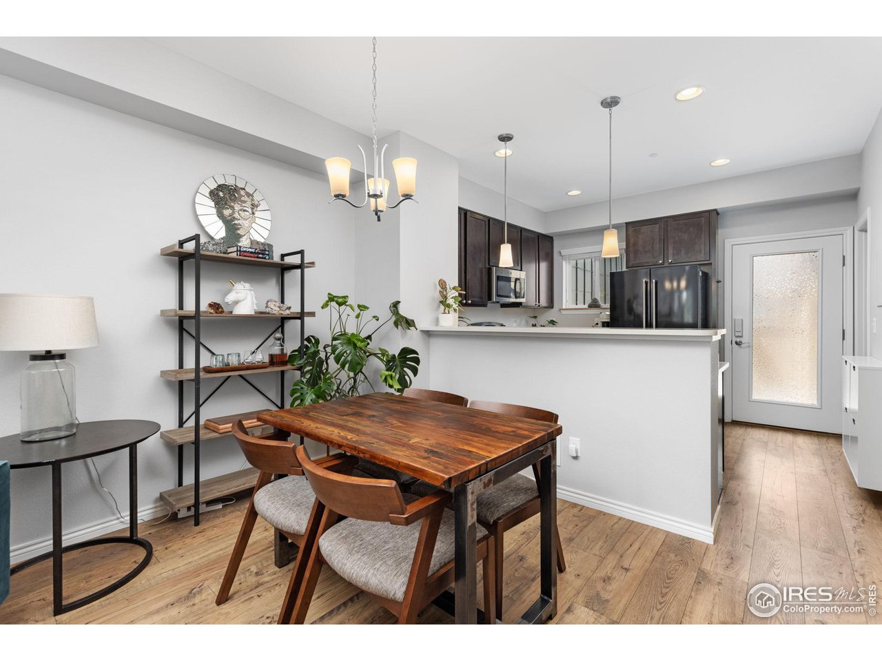 Dining area with a rustic wood table beside an open kitchen with dark cabinets and stainless steel appliances.