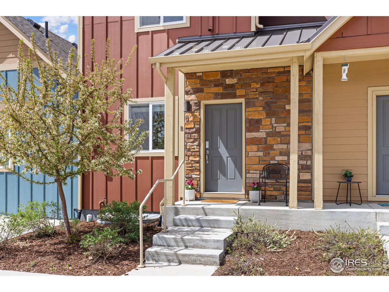 Home entrance with stone façade, covered porch, gray door, and flowering tree.
