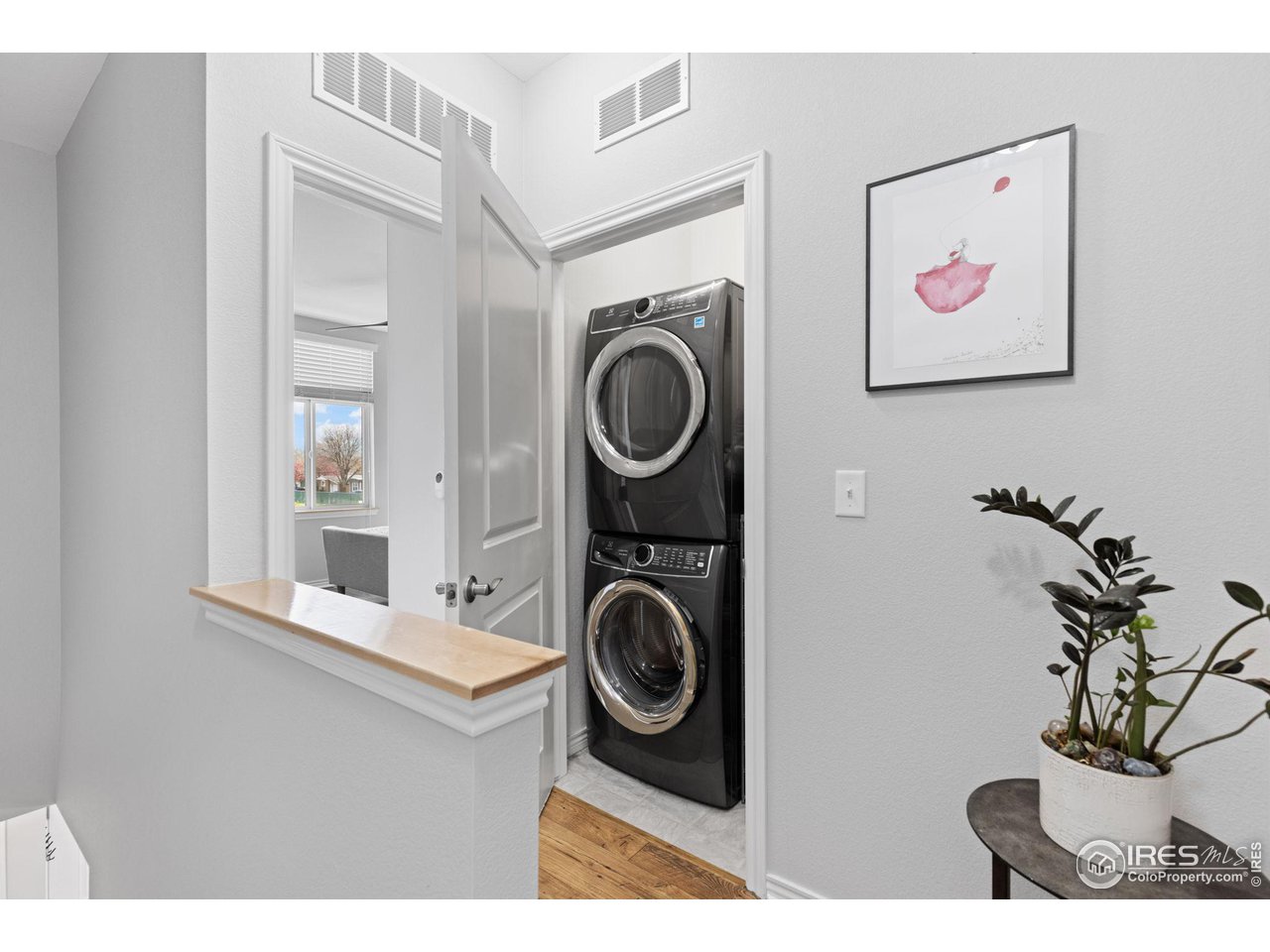 Laundry area with a stacked washer and dryer behind an open door, beside a wood-topped half wall.