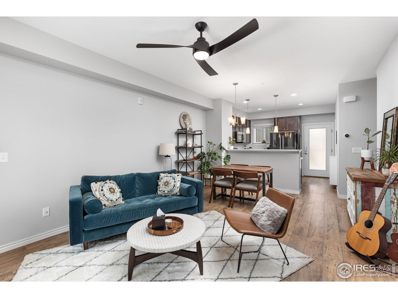 Open-plan living room with a teal sofa, round coffee table, and dining area beside the kitchen.
