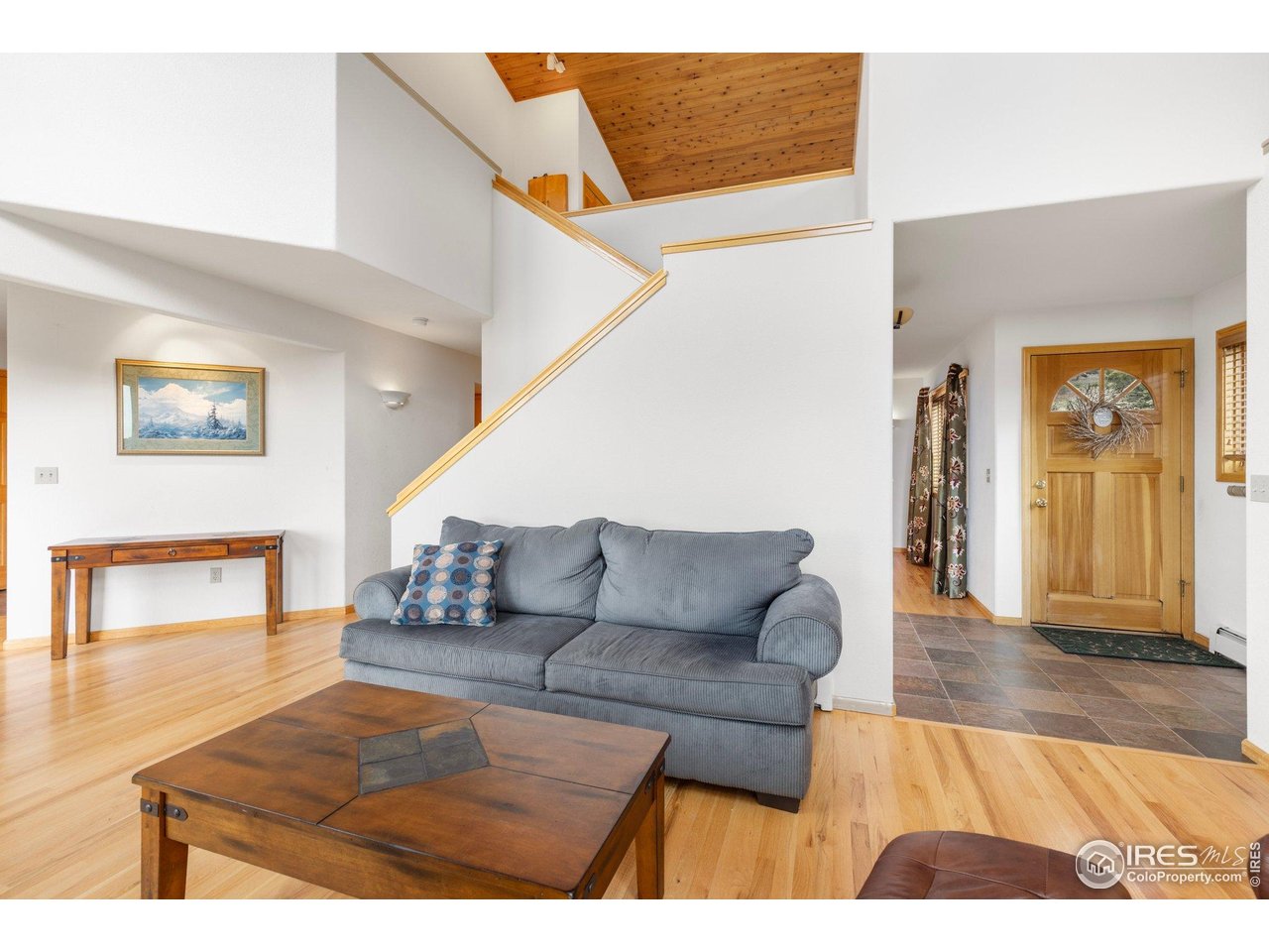 Living room with gray sofa, wood coffee table, and staircase beside the tiled entryway.