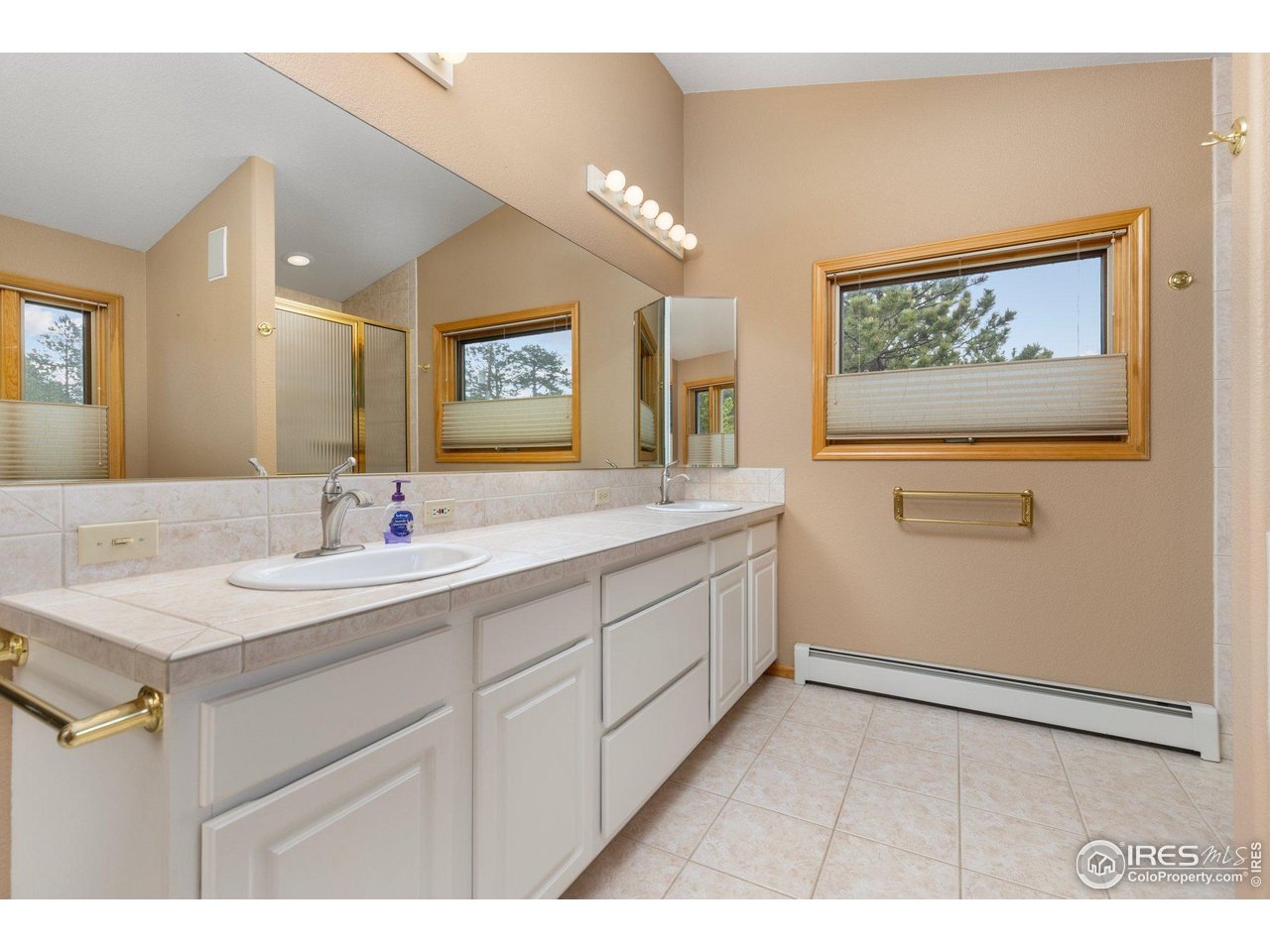 Bathroom with a long double-sink vanity, large mirror, and wood-trimmed window overlooking trees.