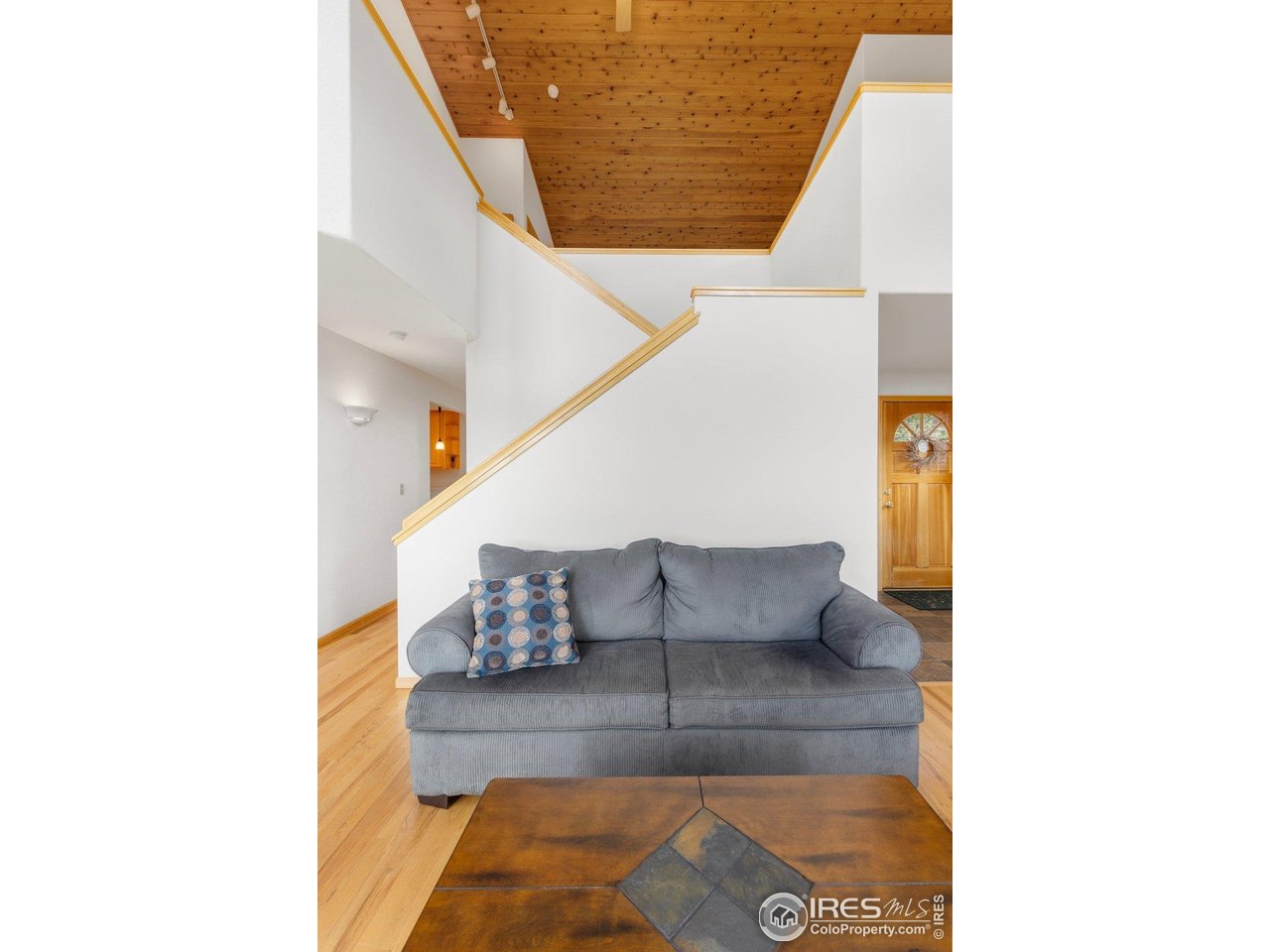 Living room with a gray sofa beneath a vaulted wood-plank ceiling and staircase.