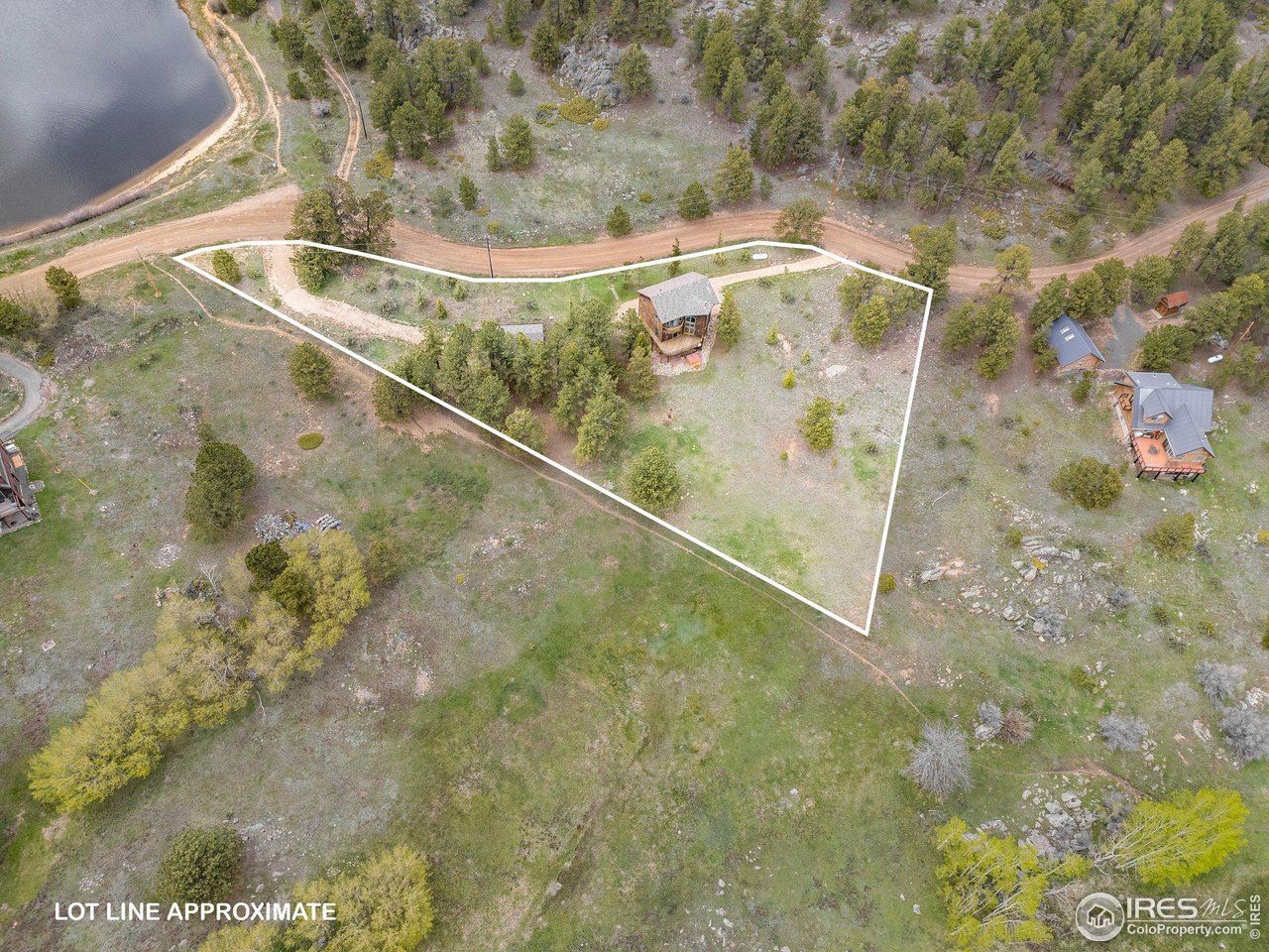 Aerial view of a wooded residential lot outlined near a lake, with a small house and road.