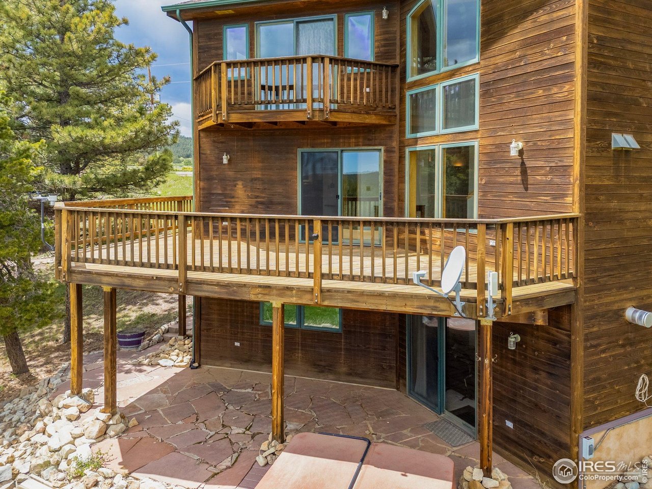 Wood-sided home with a broad elevated deck, upper balcony, and stone patio beneath.
