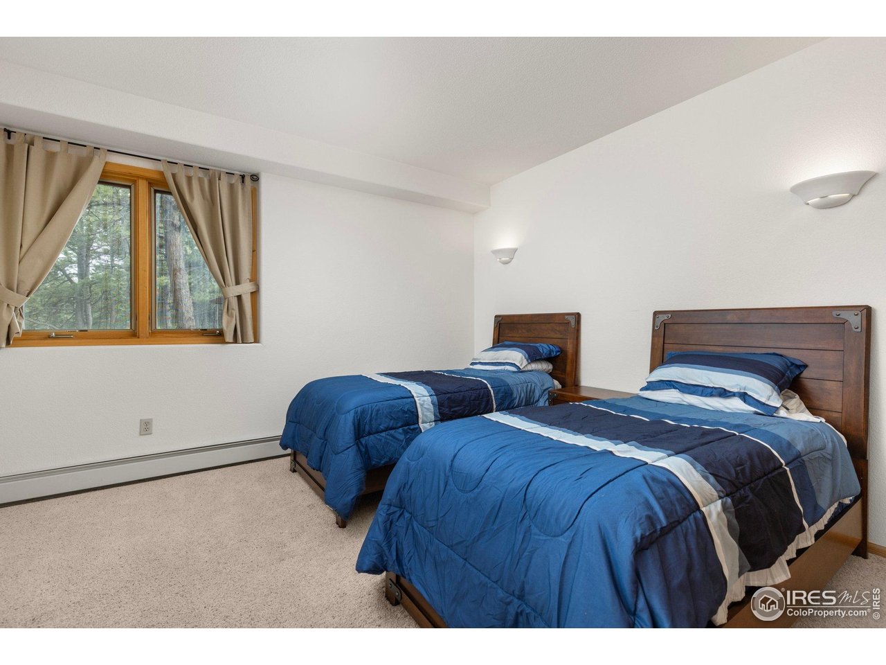 Bedroom with two blue-covered twin beds and a window overlooking trees.