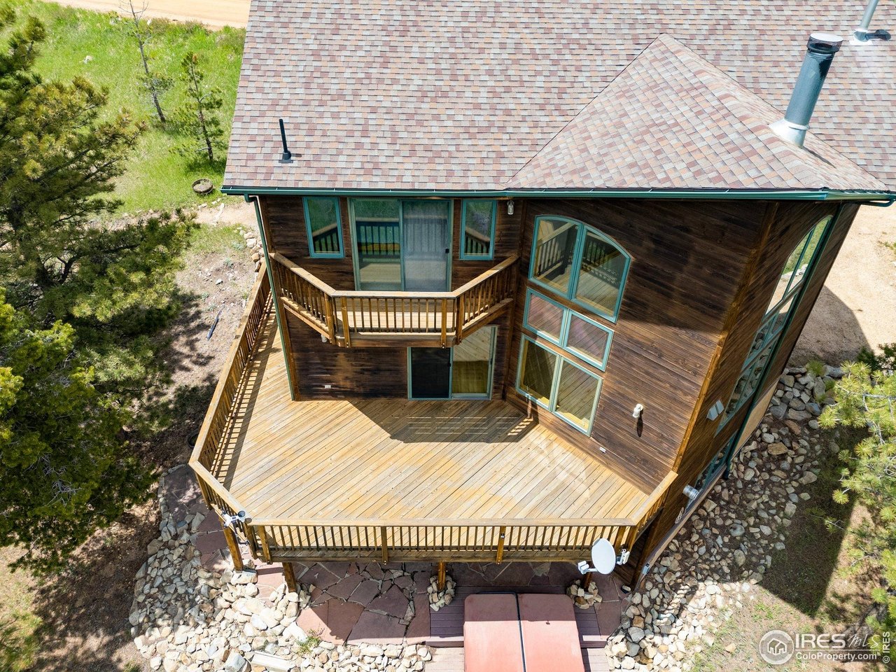 Wood-sided home with a large wraparound deck and turquoise-trimmed windows, viewed from above.
