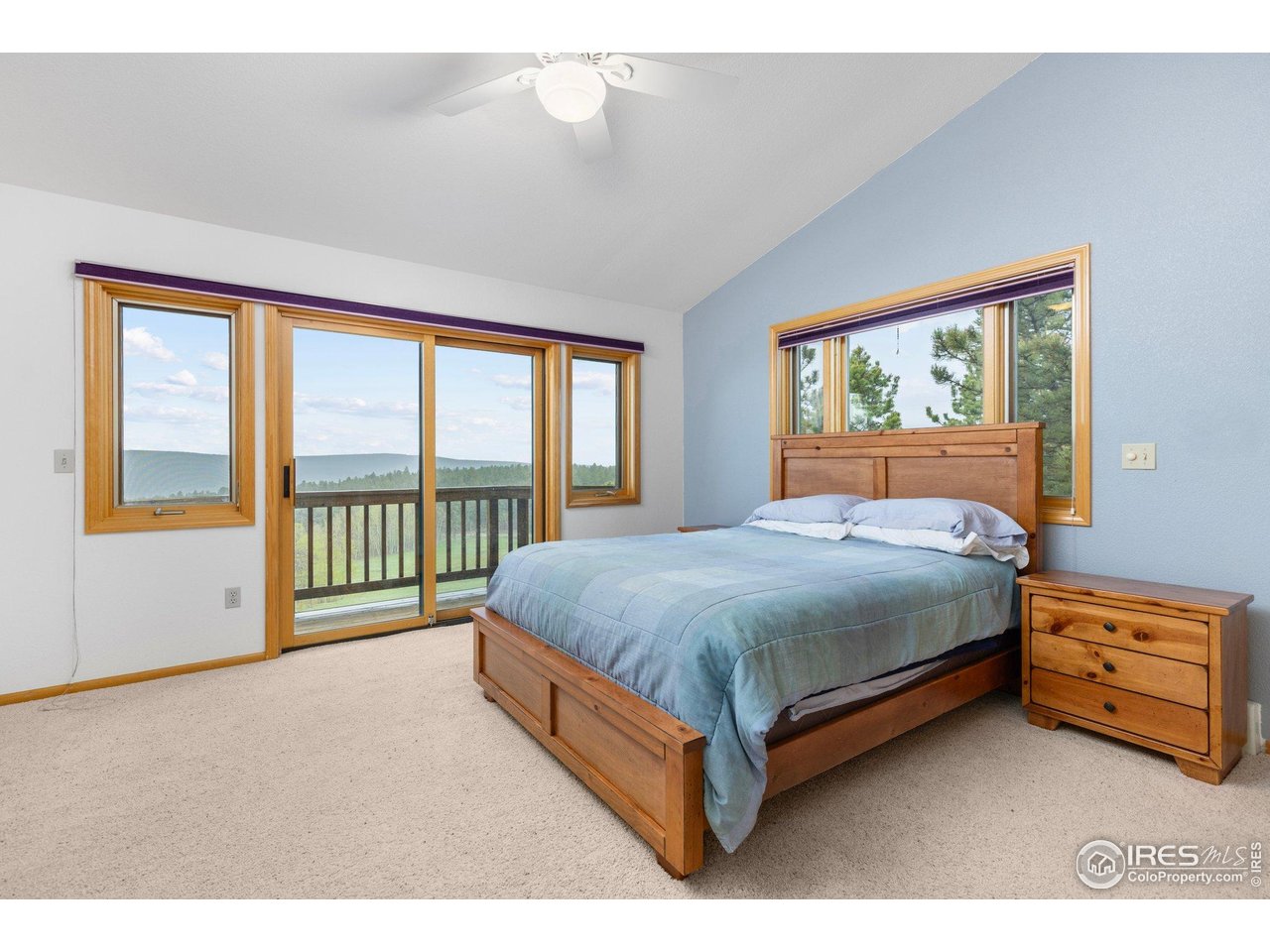Bedroom with a wooden bed and large windows overlooking wooded hills and a balcony.