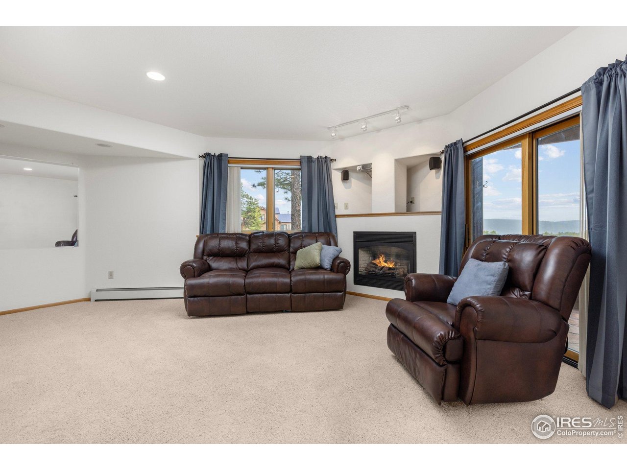 Furnished living room with leather seating, a lit fireplace, and large windows overlooking a distant water view.