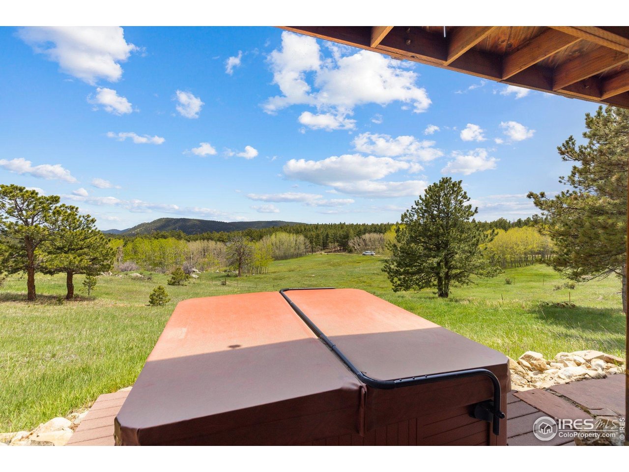 Hot tub on a covered deck overlooking a grassy meadow, pine trees and wooded hills.