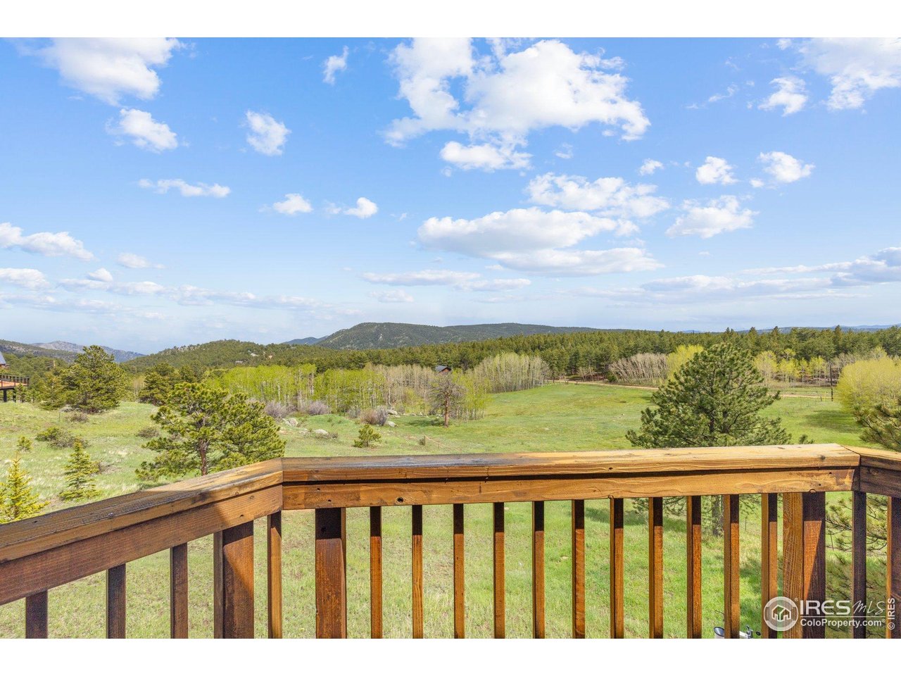 Meadow and forested mountain ridges viewed over a wooden deck railing.