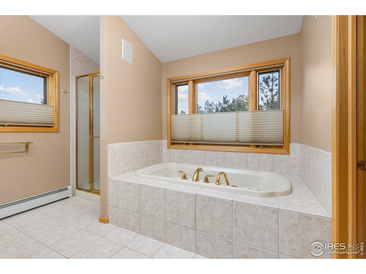 Bathroom with a tiled jetted tub beneath a large wood-trimmed window overlooking trees.