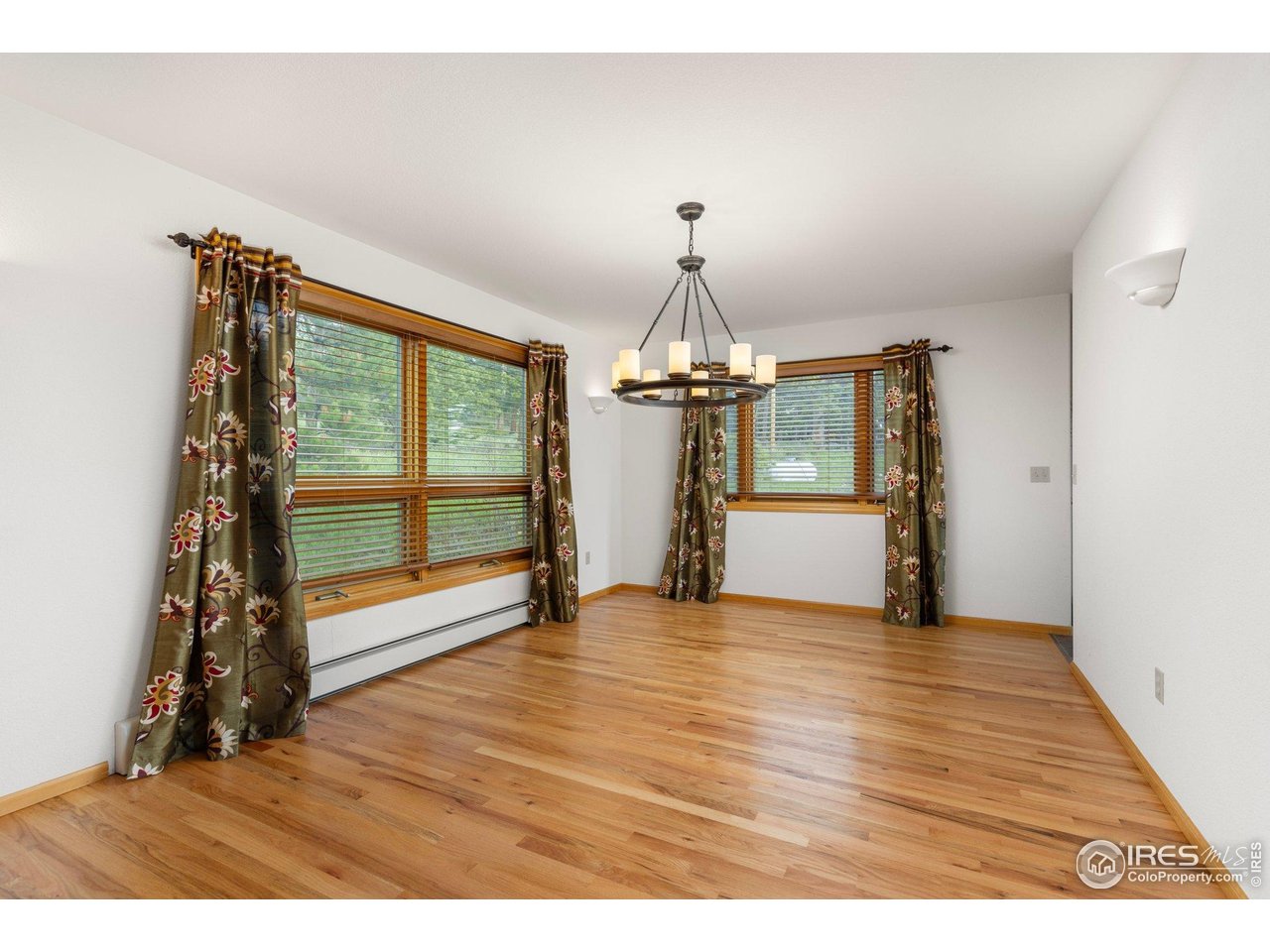 Unfurnished dining room with hardwood floors, curtained windows, and a hanging chandelier.