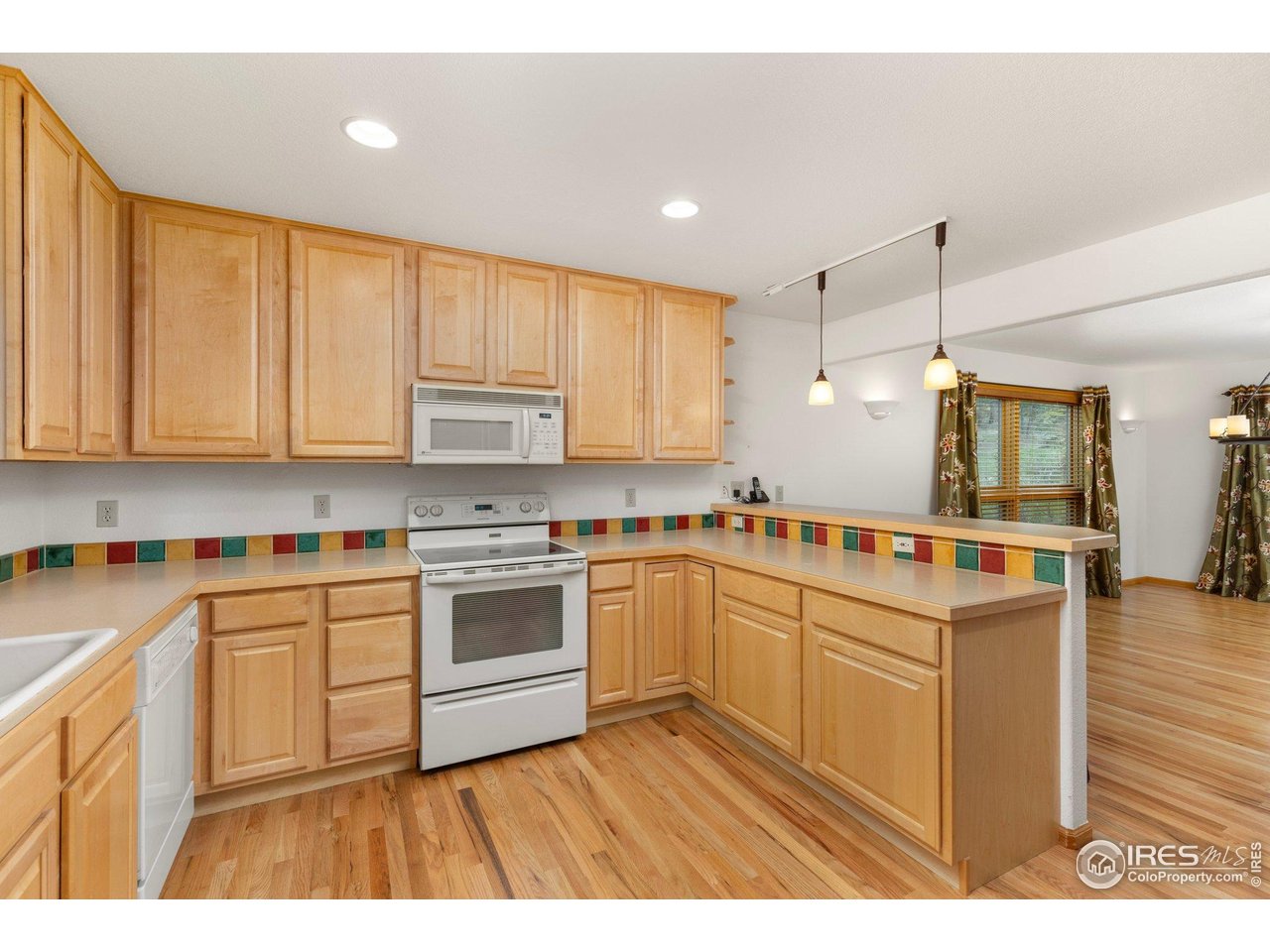 Kitchen with honey-colored wood cabinetry, colorful tile backsplash, and hardwood floors.