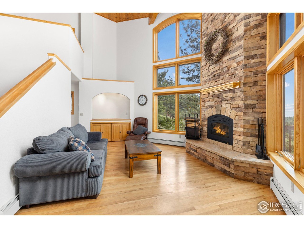 Living room with a tall stone fireplace, vaulted ceiling, and expansive wood-framed windows.