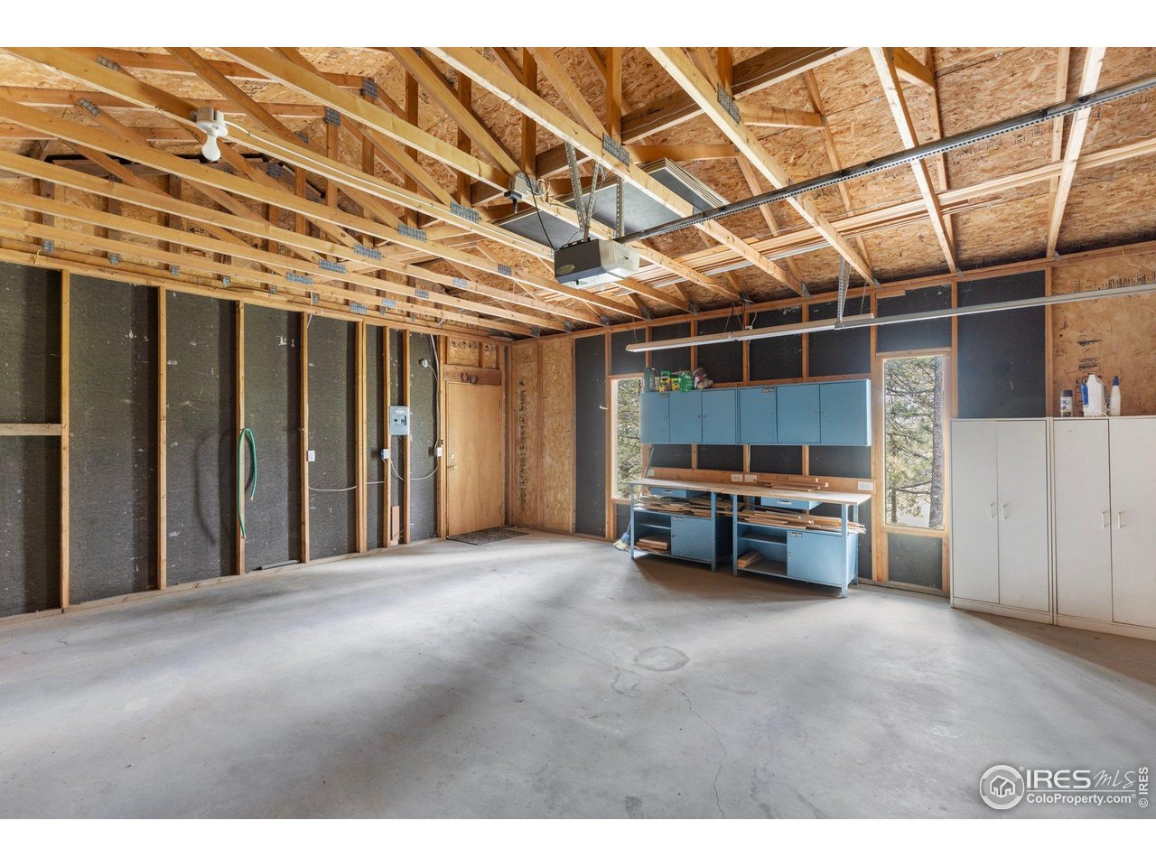 Unfinished garage with exposed roof trusses, concrete floor, and blue workshop cabinets.