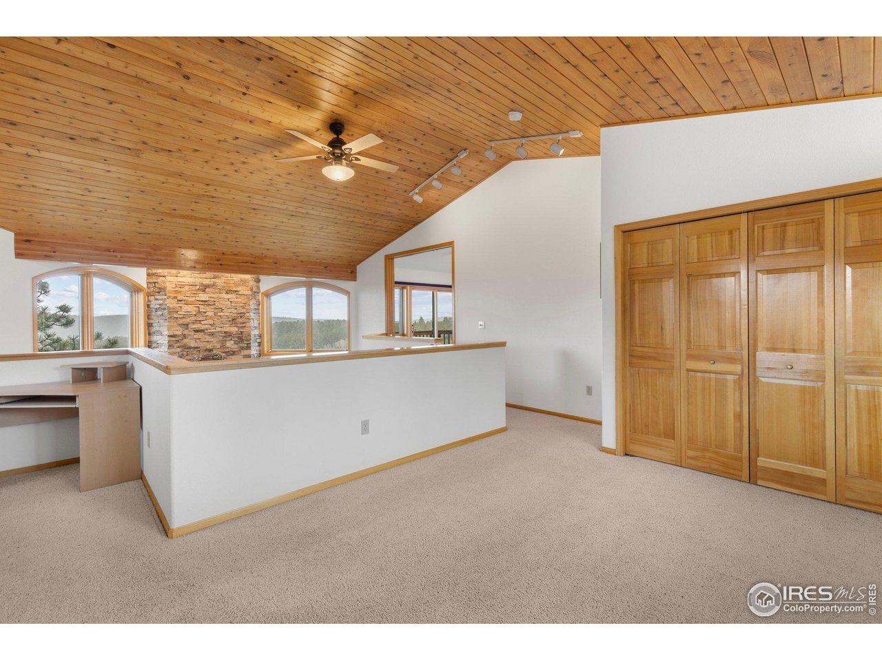 Upper-level room with a vaulted wood ceiling, built-in closets, stone accent wall, and arched windows.