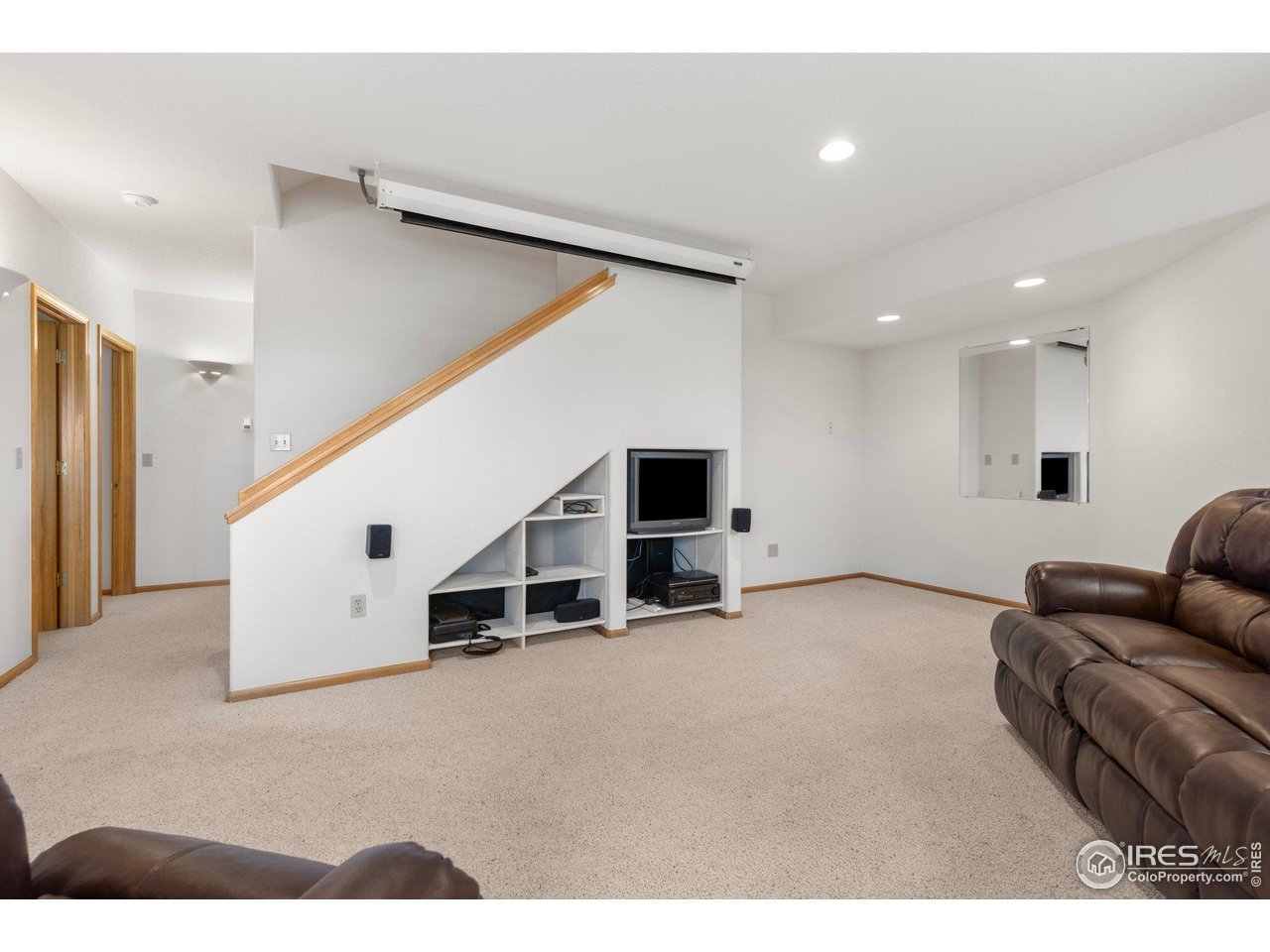 Carpeted lower-level living room with a staircase, built-in TV shelving, projection screen, and leather seating.