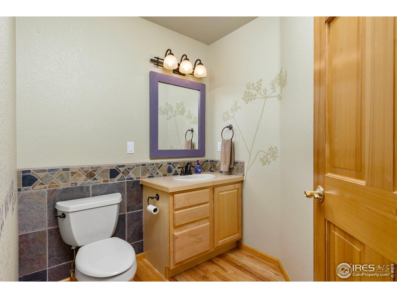 Bathroom with a wood vanity, colorful tiled backsplash, framed mirror, and white toilet.