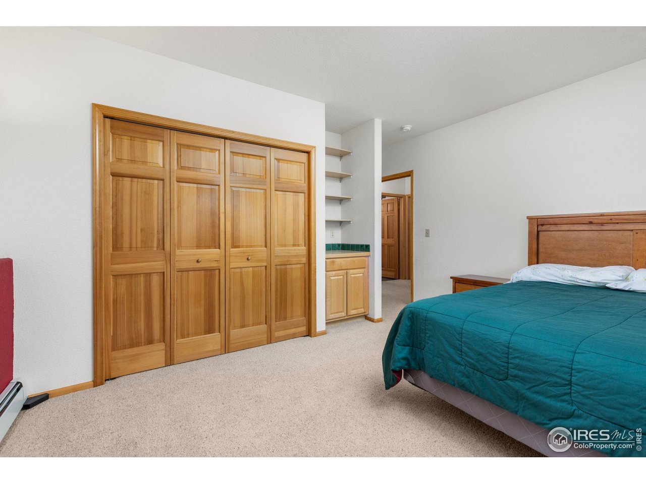 Bedroom with a teal-covered bed and honey-colored wooden closet doors.