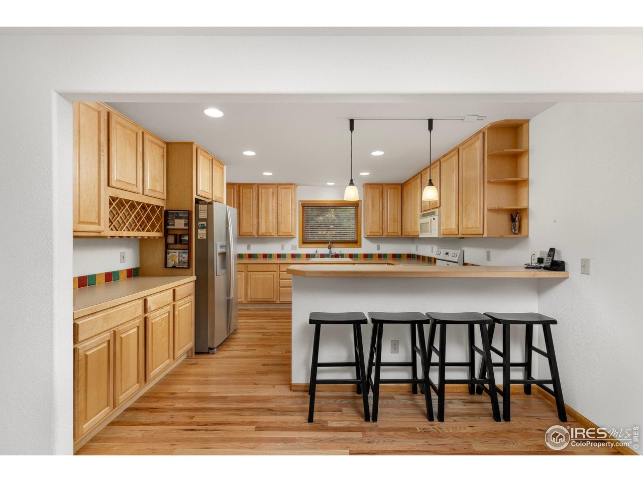 Kitchen with light wood cabinets, colorful tile backsplash, and a breakfast bar with four stools.