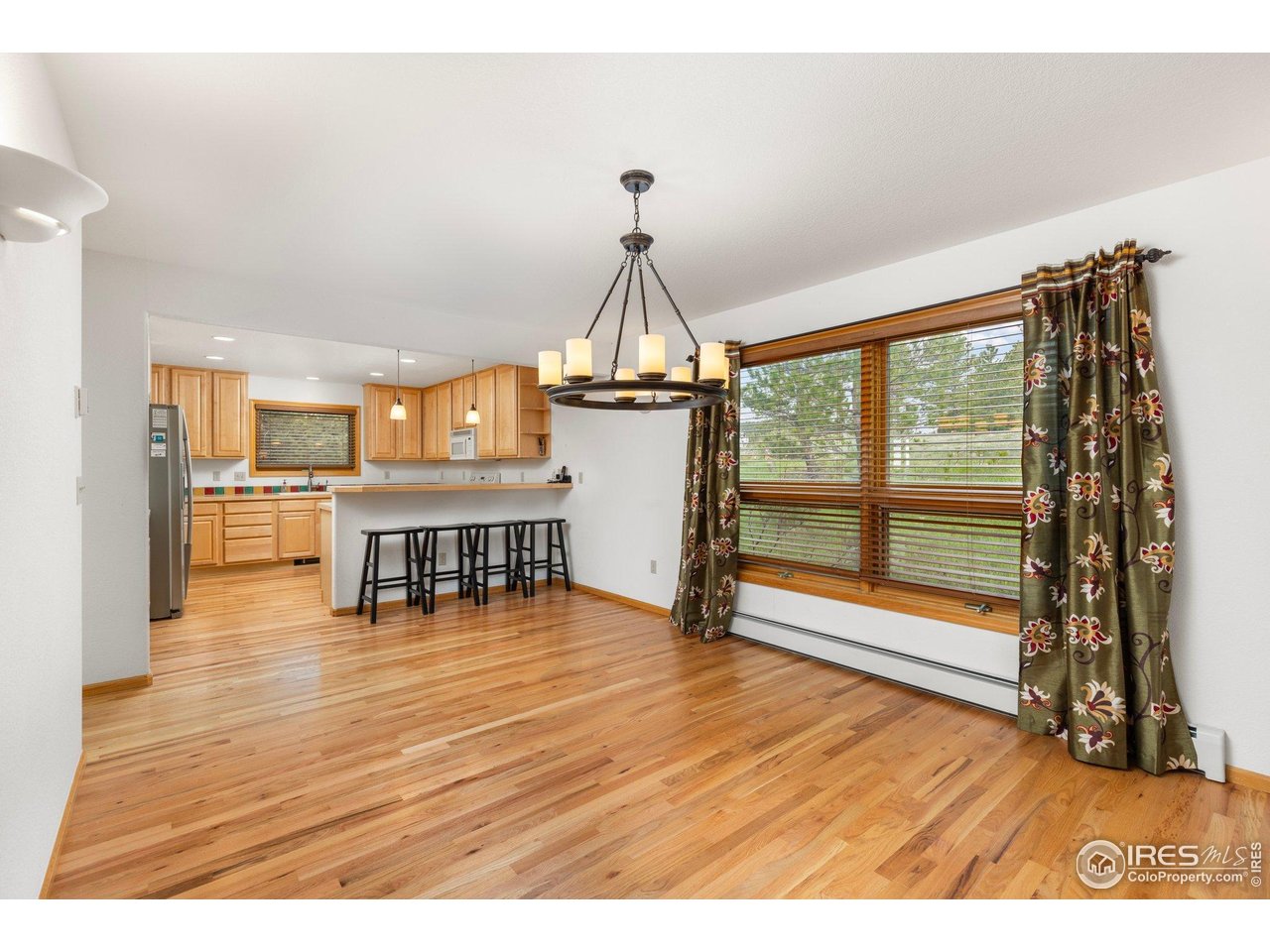 Open dining area and kitchen with hardwood floors, a breakfast bar, and a large curtained window.