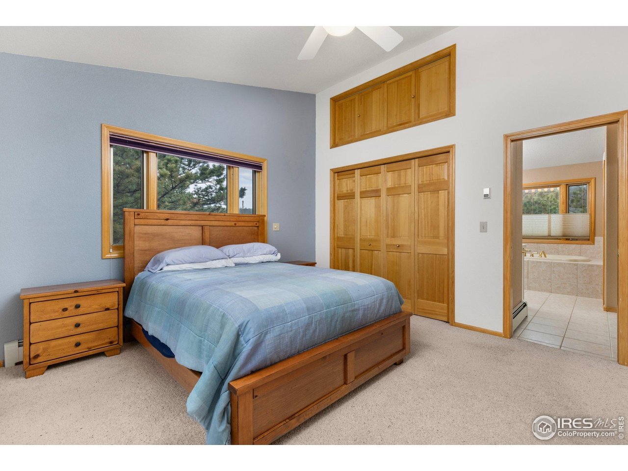 Bedroom with blue bedding, wooden furniture, and a window overlooking trees.