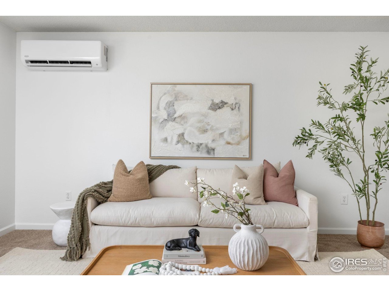 Staged living room with a white sofa, abstract wall art, and a wall-mounted mini-split air conditioner.