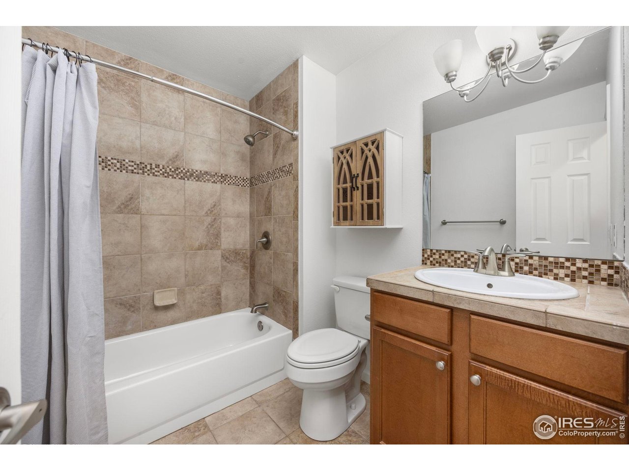 Bathroom with a tiled tub and shower, striped curtain, toilet, and wood vanity.