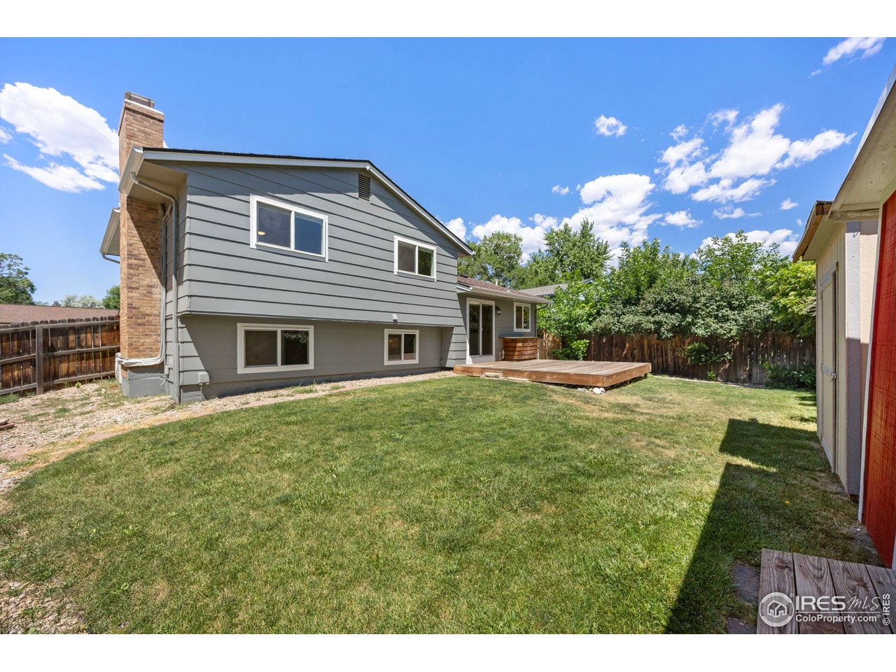 Gray split-level home viewed from the backyard, with a wooden deck and broad lawn.