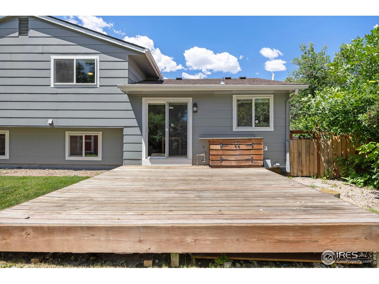 Gray-sided house with a wide wooden deck and fenced backyard.
