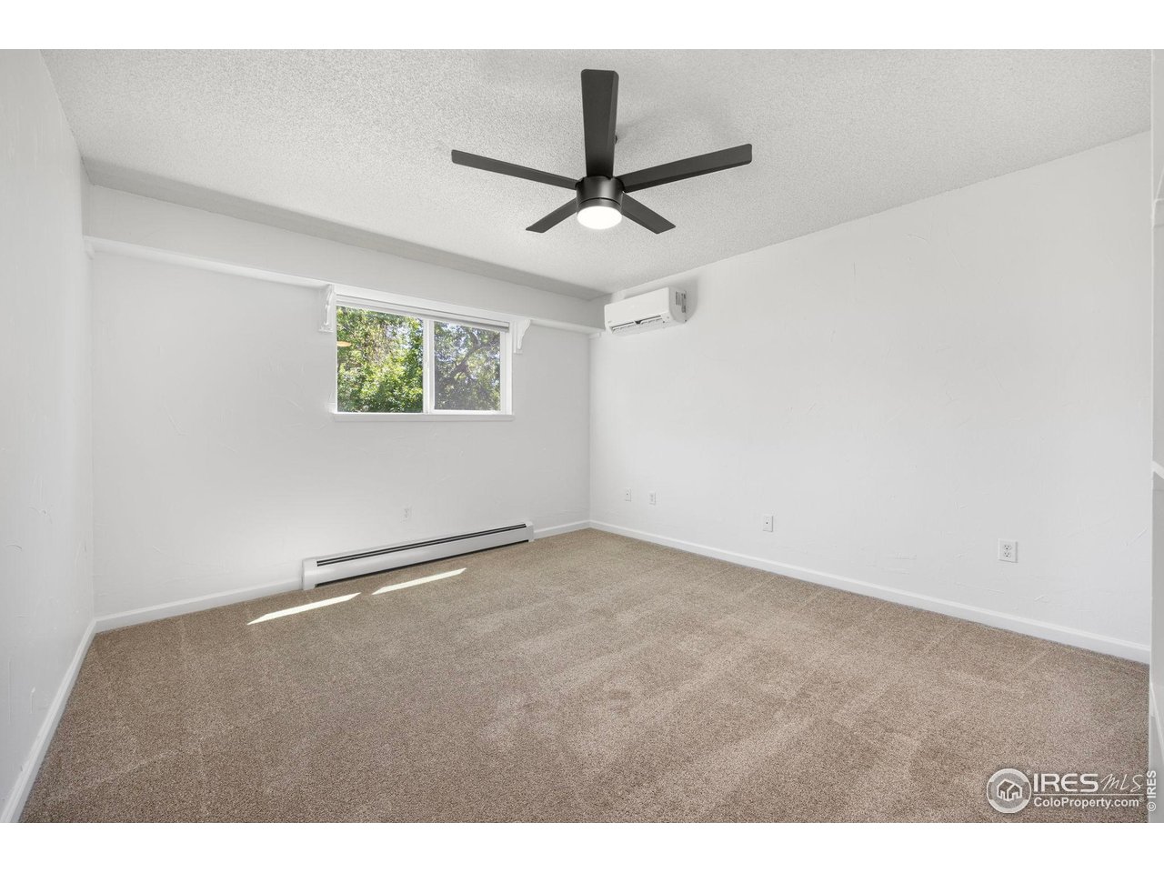 Empty carpeted bedroom with a ceiling fan, small window, and wall-mounted mini-split.