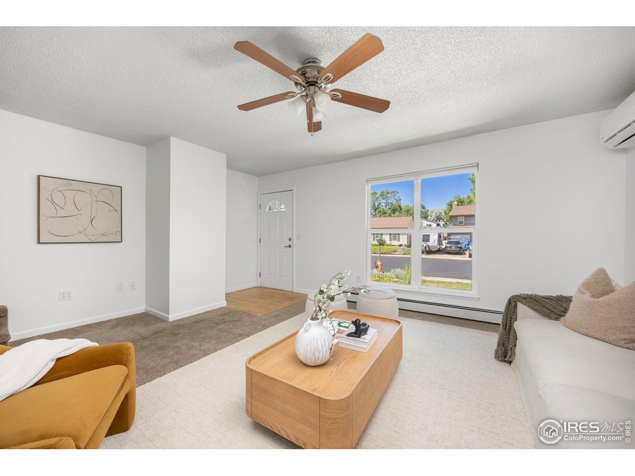 Staged living room with a ceiling fan, large window, and light wood coffee table.