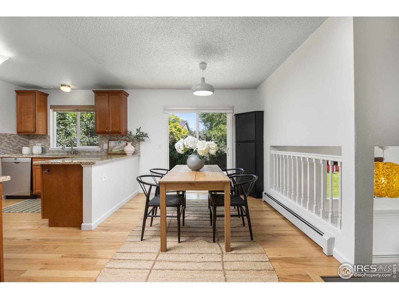Dining area with a wooden table beside the kitchen and windows overlooking greenery.