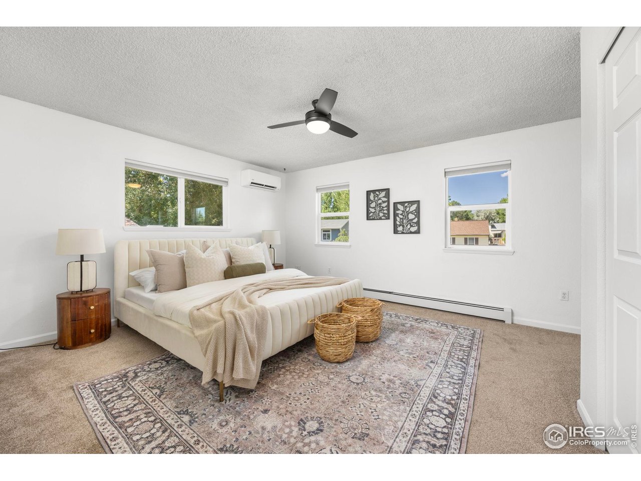 Furnished bedroom with a cream bed, patterned rug, ceiling fan, and multiple windows.