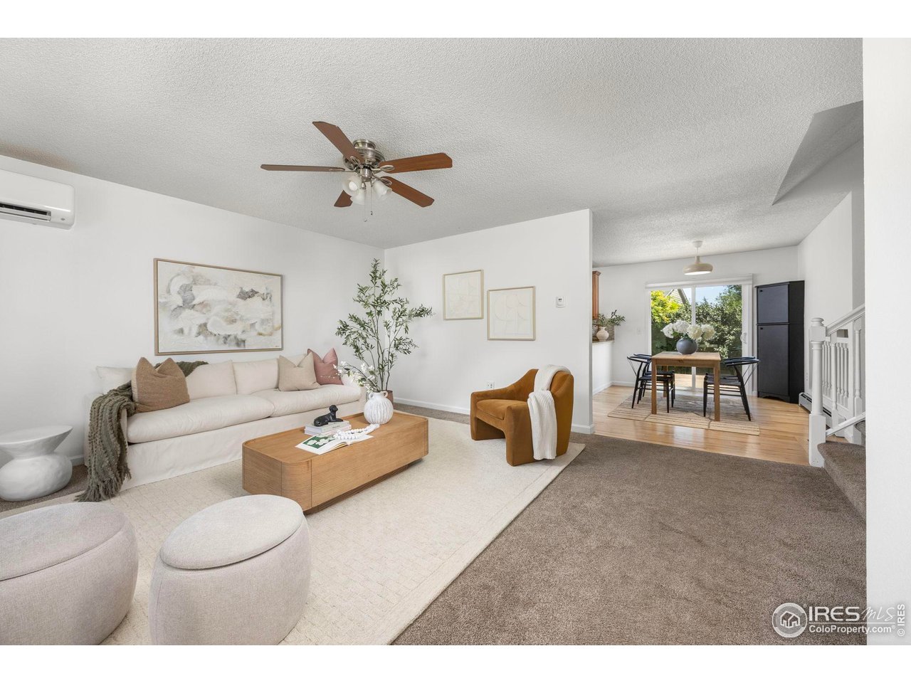 Staged living room with a white sofa and wood coffee table, opening into a sunny dining area.