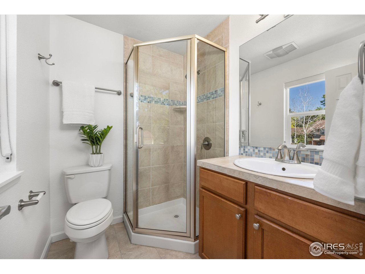 Bathroom with a glass corner shower, blue mosaic tile accent, white toilet, and wood vanity.