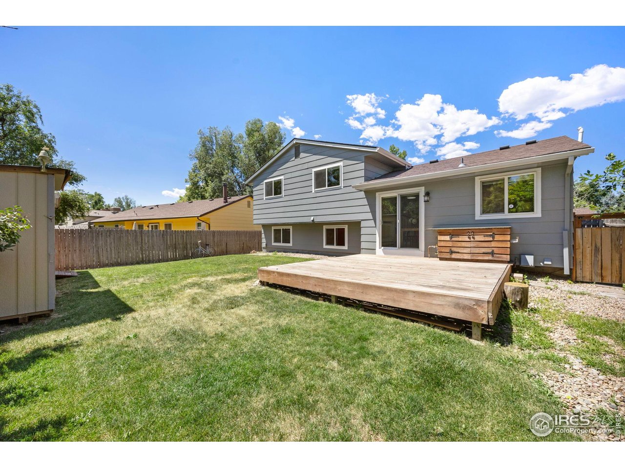 Gray split-level home with a raised wooden deck overlooking a fenced backyard lawn.